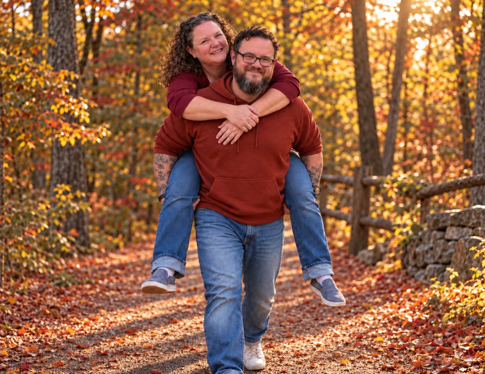 Dean giving Christa a piggyback ride on a leafy autumn trail, both smiling.